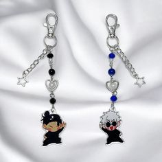 two key chains with charms attached to them on a white cloth background, one has an anime character and the other has a heart shaped charm