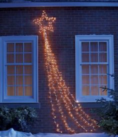 a lighted christmas tree in front of a brick building with two windows and snow on the ground