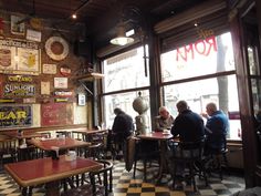 people sitting at tables in a restaurant with signs on the wall and windows above them