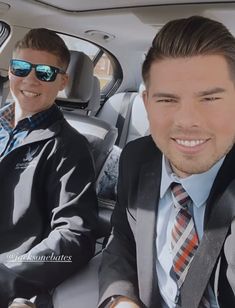 two men sitting in the back seat of a car, one with sunglasses on his head