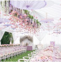 an outdoor wedding setup with pink and purple flowers hanging from the ceiling, white chairs and tables