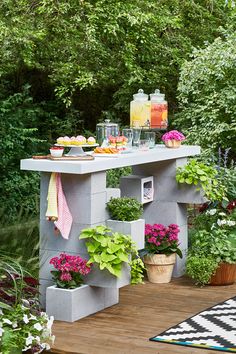 an outdoor table with potted plants and drinks on it in front of some trees