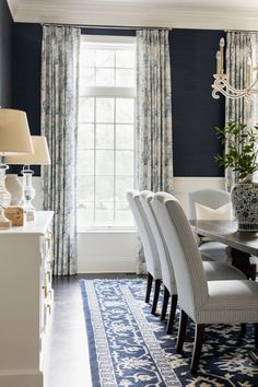 a dining room with blue walls, white chairs and a rug in front of the table