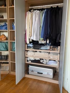 an open closet with clothes and shoes on the shelves, next to a wooden floor