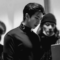 black and white photograph of young man with ear buds looking at his laptop while others look on