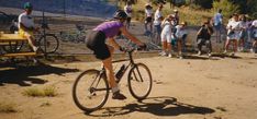 a man riding a bike down a dirt road next to a group of people watching