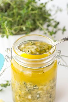 a jar filled with lemon and herbs on top of a white table next to two spoons