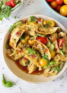 a bowl filled with pasta and vegetables next to a bowl of tomatoes on the table