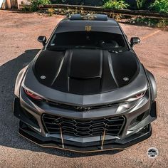 the front end of a black sports car parked in a parking lot next to trees