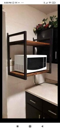 a white microwave oven sitting on top of a wooden shelf next to a black cabinet