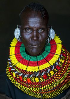 an african woman with ear rings on her neck and headdress, looking at the camera