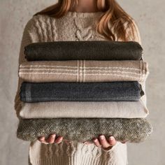 a woman is holding several blankets in her hands, all folded up and stacked on top of each other