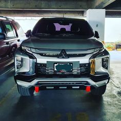 the front end of a silver and black car in a parking garage with other cars