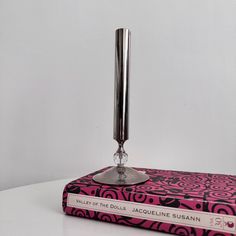 a pink and black book sitting on top of a white table next to a metal candle holder