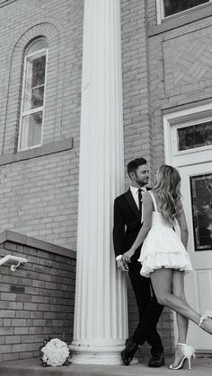 a man and woman standing next to each other in front of a tall white column