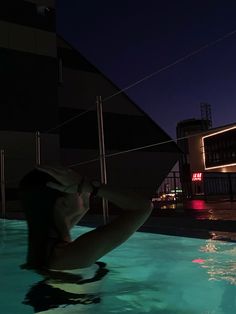 a woman in a swimming pool at night with her back turned to the camera,