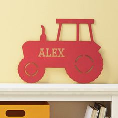 a red wooden toy tractor sitting on top of a white book shelf next to a yellow box