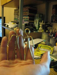 a person holding up a pair of scissors in front of a computer desk with books on it