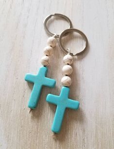 two cross key chains with beads hanging from them on a wooden surface, one is blue and the other is white