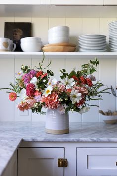 a white vase filled with lots of flowers on top of a counter next to plates and bowls