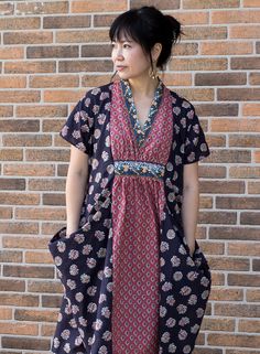 a woman standing in front of a brick wall wearing a black and red patterned dress