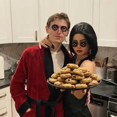 a man and woman standing next to each other holding a plate of doughnuts