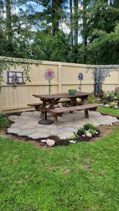 a wooden picnic table sitting in the middle of a lush green yard next to a fence