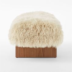 a sheepskin footstool sitting on top of a wooden block in front of a white background