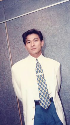 a man in a white shirt and blue tie standing next to a wall with his hands on his hips