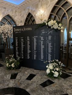 a black and white wedding seating chart with flowers on the floor in front of it