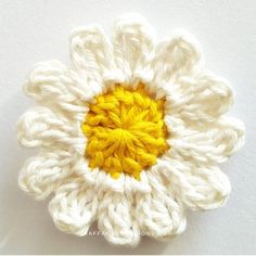 a crocheted white flower with yellow center sitting on top of a white surface