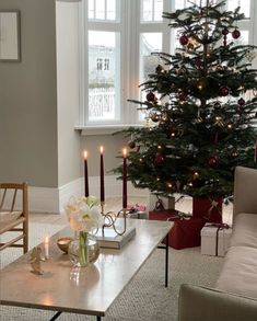 a living room with a christmas tree in the corner and candles on the coffee table