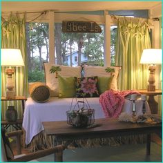 a bed sitting under a window next to two lamps and a table with pillows on it