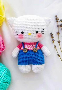 a crocheted kitty doll next to balls of yarn and some flowers on a white surface