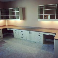 an empty room with white cabinets and counter tops in the center, is lit up by recessed lighting