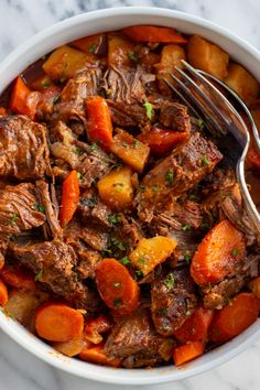 a bowl filled with beef and carrots on top of a marble counter next to a fork