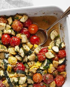 a white casserole dish filled with tomatoes, zucchini and other vegetables