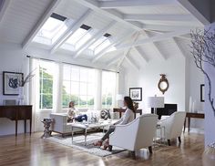 two people are sitting in the middle of a living room with white furniture and wood floors