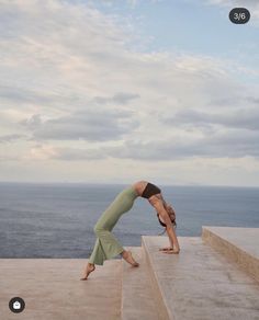 a woman is doing yoga on some steps by the ocean