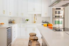 a kitchen with white cabinets and wooden stools in front of the counter top area