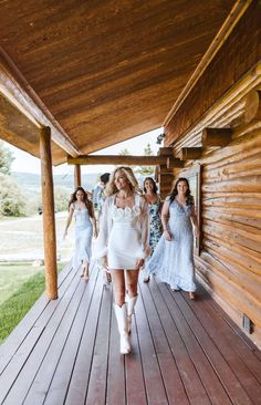 a woman walking down a wooden walkway next to other women wearing dresses and heels on the ground