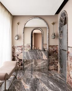 a bathroom with marble walls and flooring next to a mirror on the wall near a bench