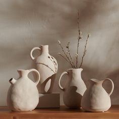 three white vases sitting on top of a wooden table next to a planter