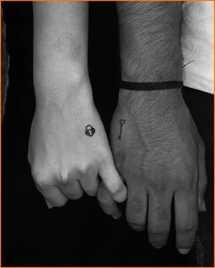 two people are holding hands with tattoos on their wrists and the other hand has a small key