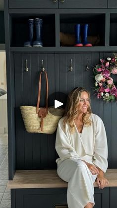 a woman sitting on a bench in front of a coat rack with flowers and purses