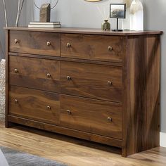 a wooden dresser sitting on top of a hard wood floor next to a mirror and lamp