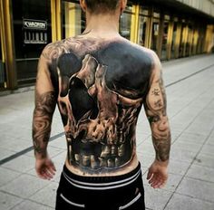 a man with tattoos on his back is standing in front of a building and looking at the street