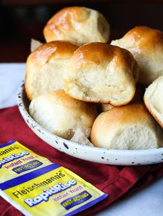 a bowl filled with rolls sitting on top of a red cloth next to a bag of butter