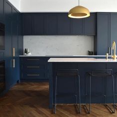 a kitchen with blue cabinets and wooden floors is pictured in this image, there are three bar stools at the center of the island