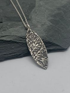 This lovely oval floral daisy necklace has been entirely handmade using .999 fine silver. It has been cut from fine silver precious metal clay, textured, fired and oxidized. The pendant hangs from a sterling silver diamond cut cable chain. This fine silver long oval pendant features an embossed daisy floral textured pattern. Pendant size: approximately 1 1/4 x 1/2 inches Chain length: adjustable at 16 and 18 inches can also be customized to whatever length needed The necklace is sent in a gift b Silver Oval Jewelry With Flower Charm, Silver Stamped Oval Pendant Necklace, Bohemian Oval Necklace Stamped 925, Oval Sterling Silver Necklace With Etched Detail, Etched Oval Sterling Silver Necklace, Artisan Oval Engraved Necklace, Artisan Engraved Oval Necklace, Nature-inspired Oval Engraved Necklaces, Nature-inspired Oval Engraved Necklace